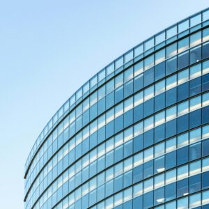 Low angle view of a modern glass office building against a clear blue sky.